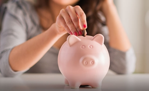 Eine Hand, die eine Münze in ein rosa Sparschwein steckt.